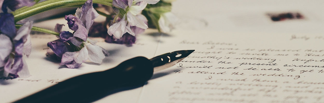 a pen and purple flowers atop a sheet of paper with cursive writing